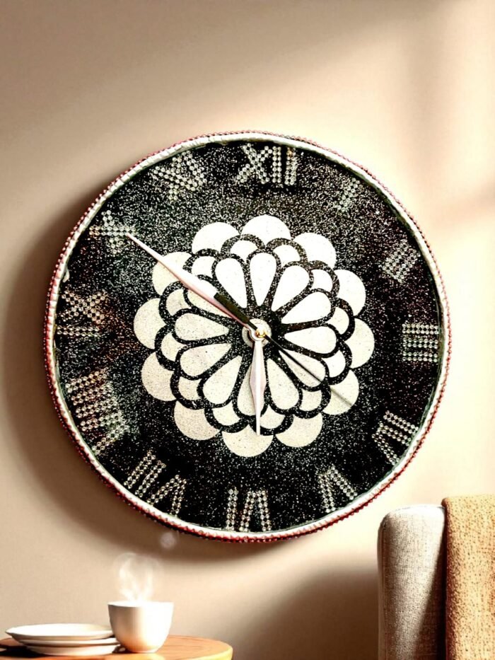 Artistic Design & Craftsmanship Kolam-Inspired Mandala Pattern: The heart of this clock features a sacred geometric floral motif, symbolizing balance, unity, and positive energy. Luxury Black & White Contrast: The bold jet-black resin base paired with shimmering white mandala details creates a striking, high-end look. Crystal Studded Roman Numerals: Each numeral is designed with embedded shimmering stones, offering sparkle and a regal touch. Intricate Resin Detailing: Hand-poured resin with precision artistry ensures a smooth glossy finish that enhances the luxurious aesthetic. Kolam Mandala Resin Clock